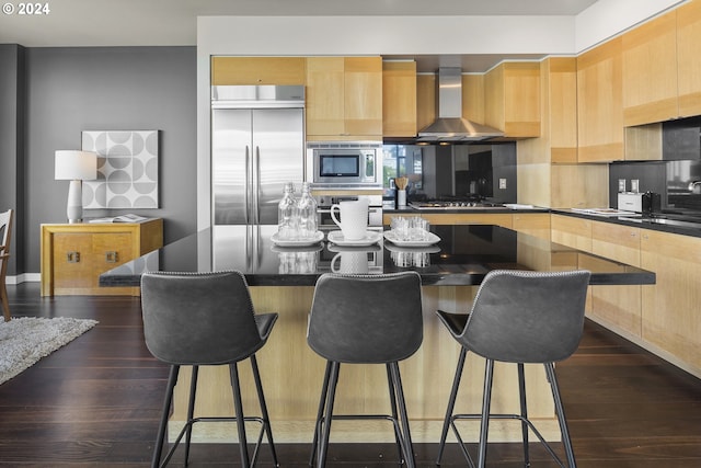 kitchen with sink, built in appliances, dark hardwood / wood-style floors, a kitchen island, and wall chimney range hood