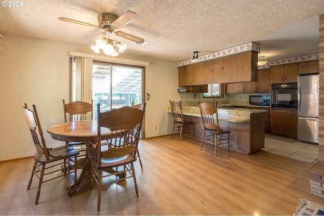 dining room with ceiling fan, baseboards, light wood finished floors, and a textured ceiling