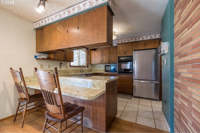 kitchen with black appliances, light countertops, a peninsula, a kitchen breakfast bar, and a textured ceiling