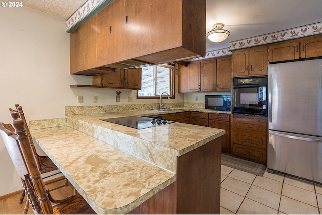 kitchen featuring a breakfast bar, a peninsula, light tile patterned flooring, a sink, and black appliances