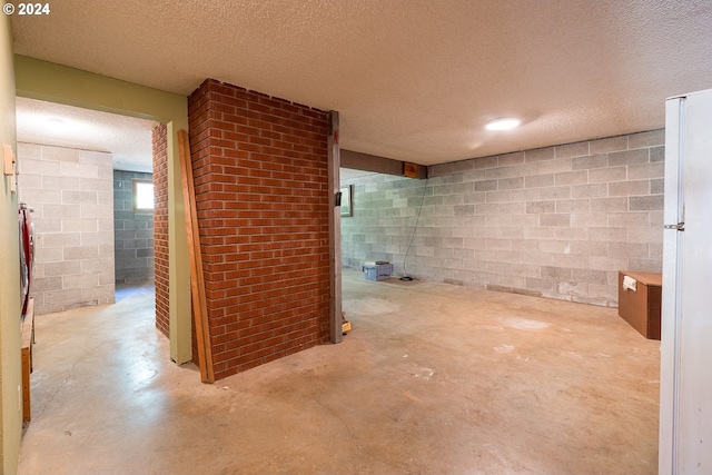 finished below grade area with a textured ceiling, concrete block wall, and freestanding refrigerator