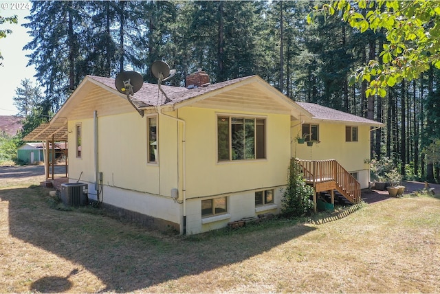 view of side of property featuring a shingled roof, a yard, central AC unit, and a chimney