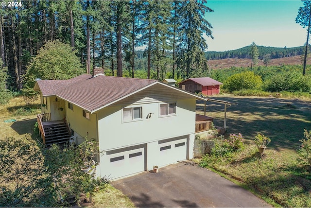 view of property exterior with driveway, a shingled roof, stucco siding, a garage, and a view of trees