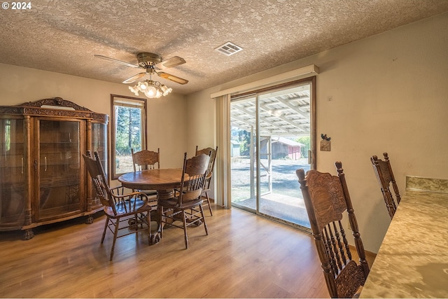 dining area with a wealth of natural light, visible vents, a textured ceiling, and light wood-style flooring