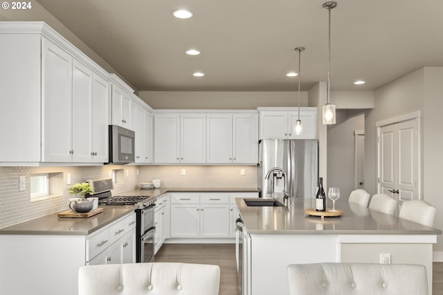 kitchen featuring appliances with stainless steel finishes, a kitchen island with sink, sink, white cabinets, and hanging light fixtures