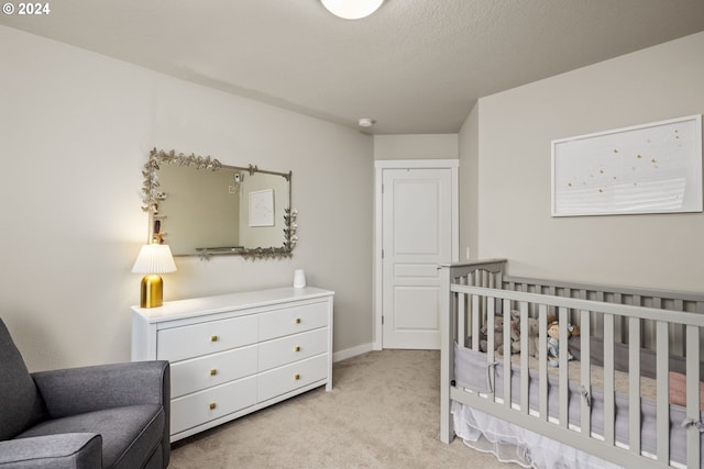 bedroom with a crib, a textured ceiling, and light colored carpet