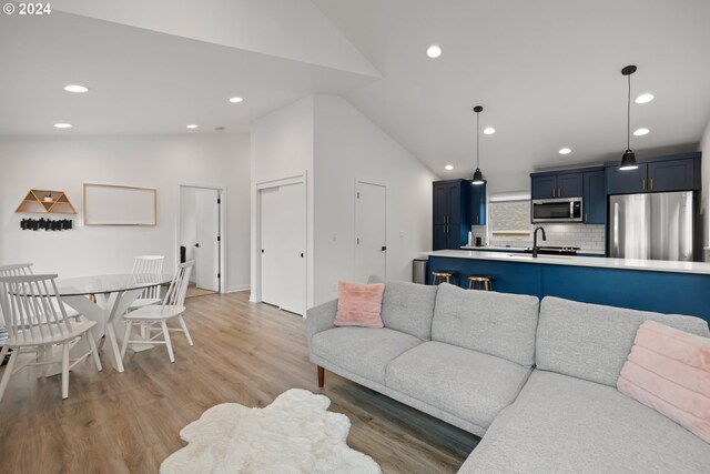 living room featuring sink, light wood-type flooring, and high vaulted ceiling