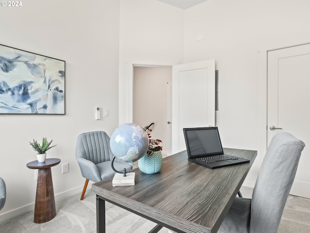 office area featuring light carpet, a towering ceiling, and baseboards