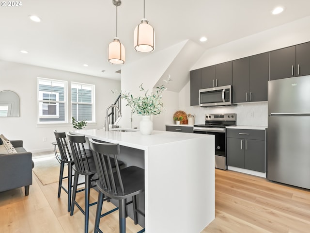 kitchen featuring appliances with stainless steel finishes, dark cabinets, a kitchen island with sink, light countertops, and pendant lighting