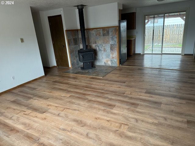 unfurnished living room featuring a wood stove, light wood-type flooring, and a textured ceiling