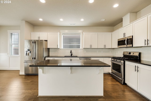 kitchen with appliances with stainless steel finishes, a kitchen island, a kitchen bar, and dark wood-type flooring