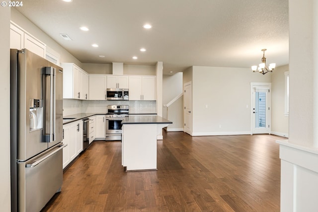 kitchen with white cabinets, decorative light fixtures, appliances with stainless steel finishes, dark hardwood / wood-style floors, and a center island