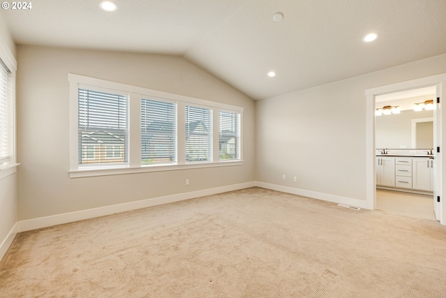 unfurnished bedroom featuring light carpet, vaulted ceiling, and ensuite bathroom