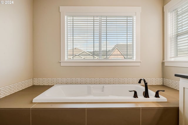 bathroom featuring a healthy amount of sunlight, vanity, and tiled bath