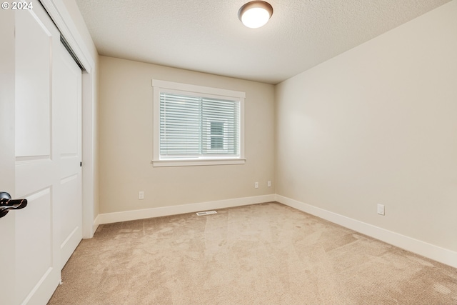 unfurnished bedroom featuring a closet, a textured ceiling, and light carpet