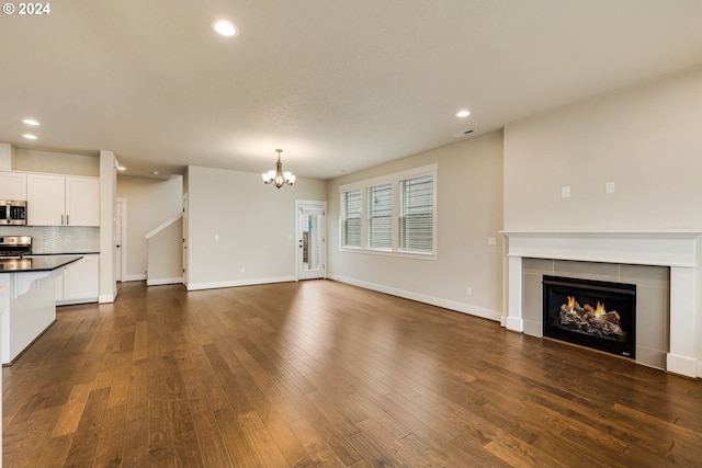 unfurnished living room with dark wood-type flooring, a notable chandelier, and a tile fireplace