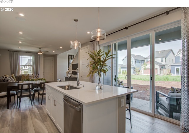 kitchen featuring dishwasher, light wood-type flooring, pendant lighting, white cabinets, and a center island with sink