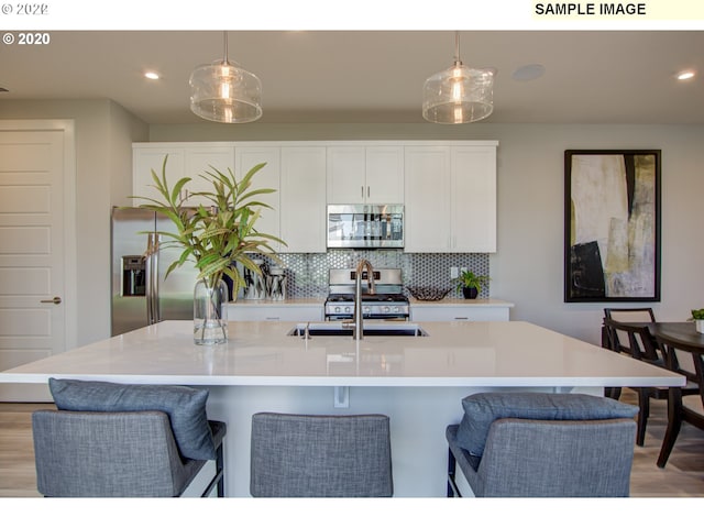 kitchen featuring appliances with stainless steel finishes, an island with sink, light wood-type flooring, and pendant lighting