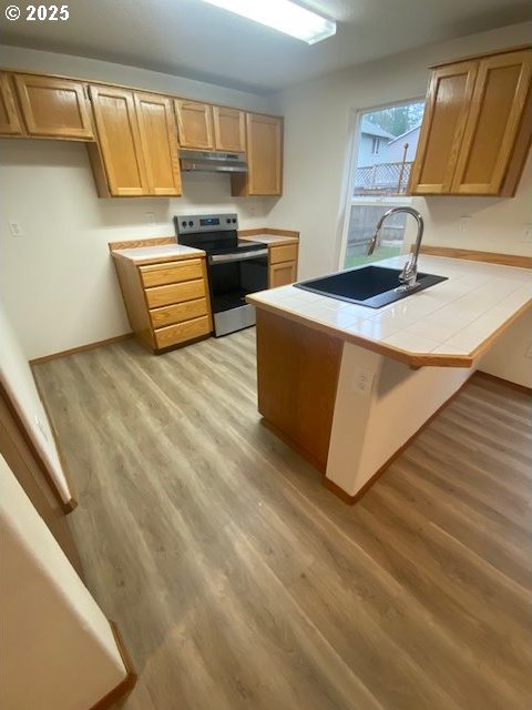 kitchen featuring stainless steel electric stove, sink, light hardwood / wood-style flooring, tile counters, and kitchen peninsula