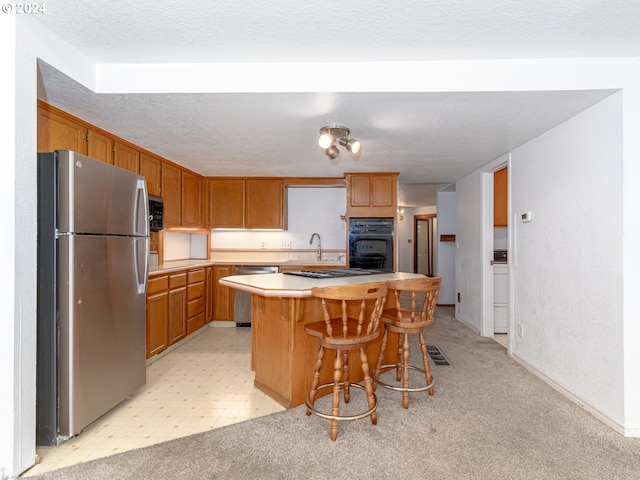 kitchen featuring a center island, light countertops, appliances with stainless steel finishes, brown cabinetry, and a kitchen bar