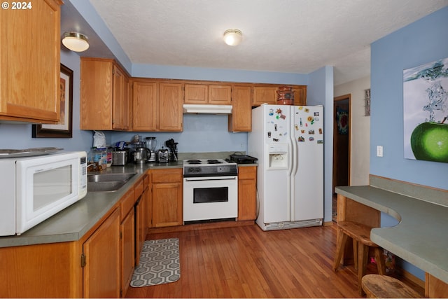 kitchen with light wood-type flooring, white appliances, sink, and a textured ceiling