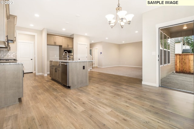 kitchen featuring light wood-type flooring, backsplash, stainless steel appliances, pendant lighting, and a kitchen island with sink