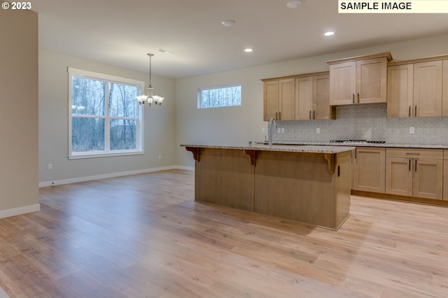 kitchen with a center island with sink, light stone countertops, light brown cabinetry, light hardwood / wood-style floors, and sink