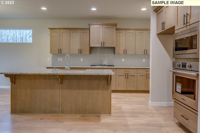 kitchen with light hardwood / wood-style flooring, an island with sink, light stone counters, and stainless steel appliances