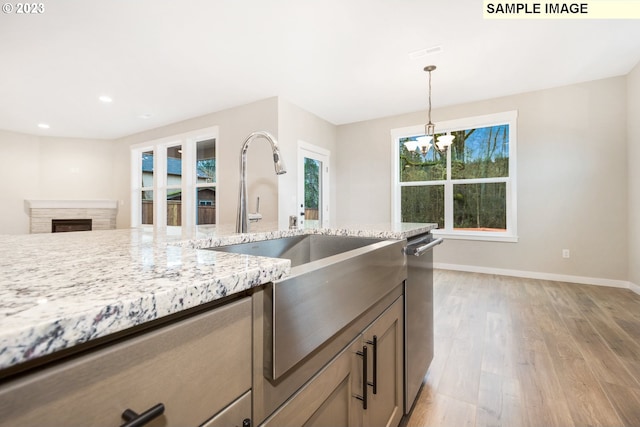 kitchen featuring hanging light fixtures, light hardwood / wood-style floors, stainless steel dishwasher, light stone counters, and a notable chandelier