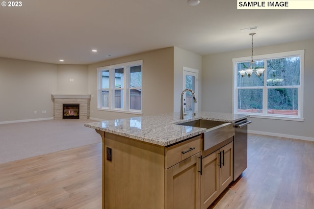 kitchen featuring sink, an island with sink, hanging light fixtures, stainless steel dishwasher, and light stone counters