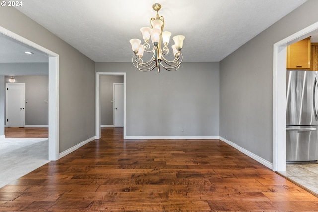 unfurnished dining area with a textured ceiling, a chandelier, and dark hardwood / wood-style flooring