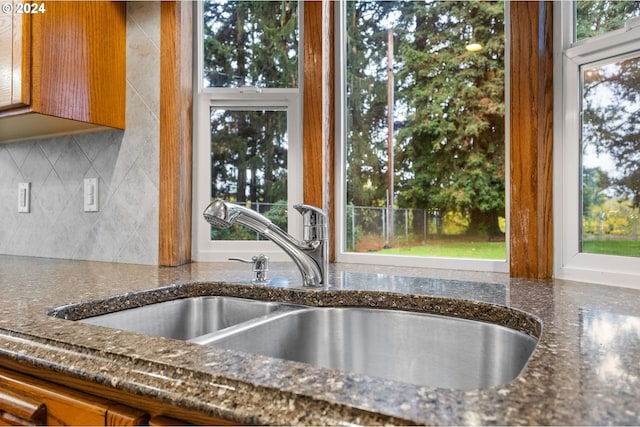 kitchen featuring a wealth of natural light, sink, dark stone counters, and tasteful backsplash