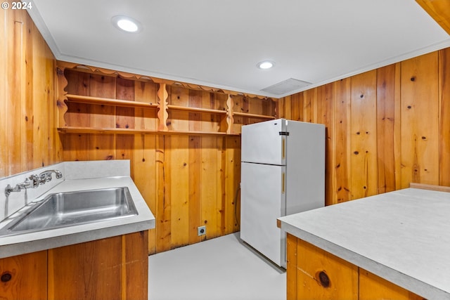 kitchen featuring ornamental molding, wooden walls, sink, and white refrigerator