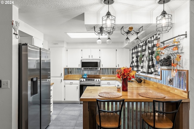 kitchen featuring butcher block countertops, white cabinetry, appliances with stainless steel finishes, and decorative light fixtures