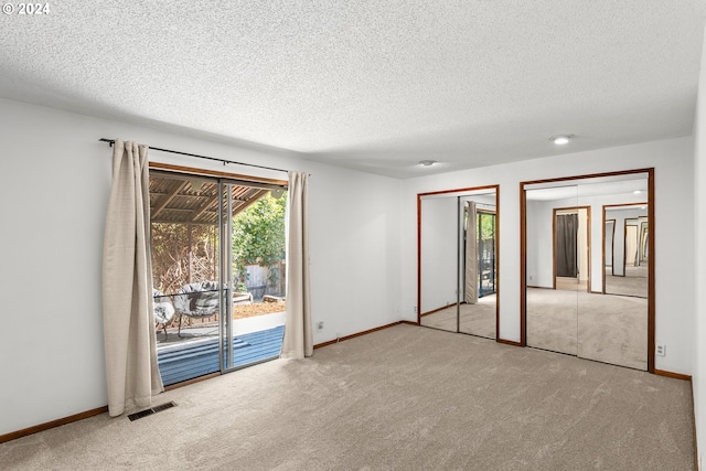 unfurnished bedroom featuring two closets, a textured ceiling, light colored carpet, and access to outside