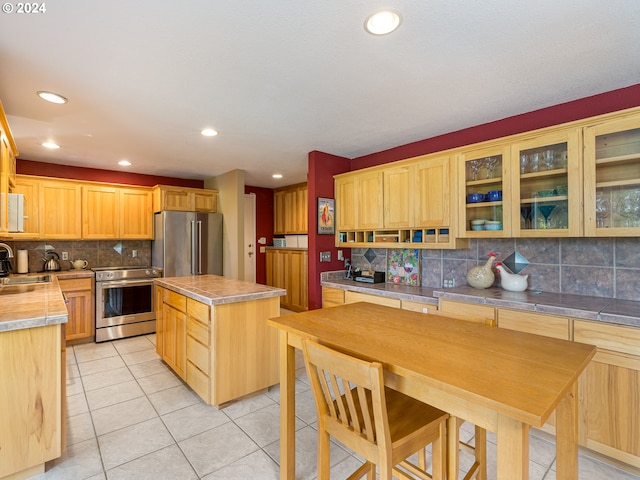 kitchen featuring appliances with stainless steel finishes, a kitchen island, sink, light tile patterned flooring, and tasteful backsplash