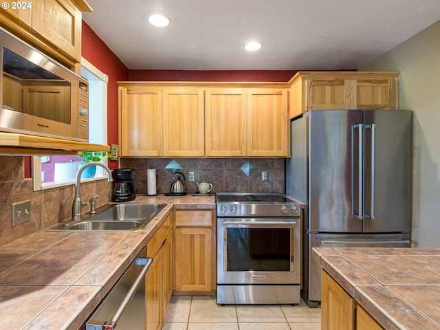 kitchen with stainless steel appliances, sink, light tile patterned floors, tile counters, and decorative backsplash