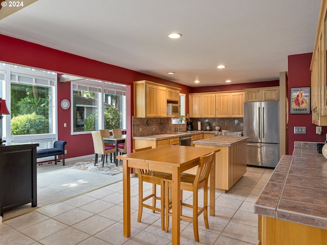 kitchen with sink, light brown cabinets, light tile patterned floors, decorative backsplash, and appliances with stainless steel finishes