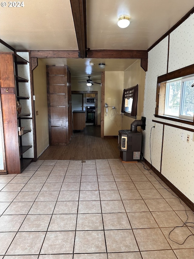 interior space featuring beam ceiling, a wood stove, and ceiling fan