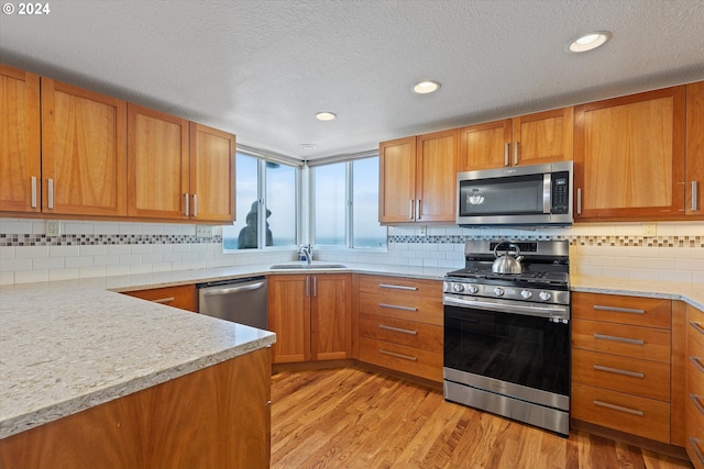 kitchen featuring light wood-type flooring, backsplash, a textured ceiling, stainless steel appliances, and sink