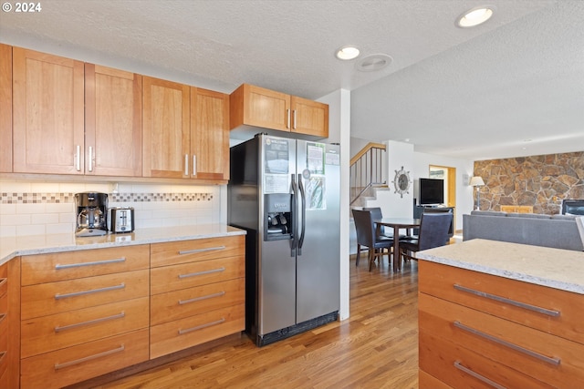 kitchen featuring light stone countertops, stainless steel refrigerator with ice dispenser, backsplash, a textured ceiling, and light wood-type flooring