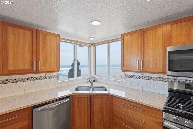 kitchen with light stone countertops, appliances with stainless steel finishes, tasteful backsplash, a textured ceiling, and sink