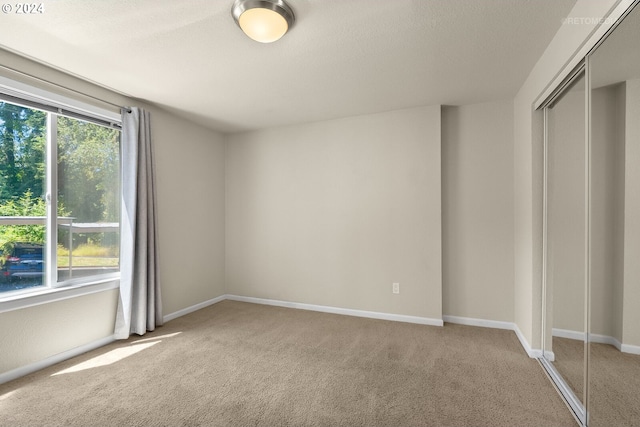 unfurnished bedroom with light carpet, a textured ceiling, a closet, and multiple windows