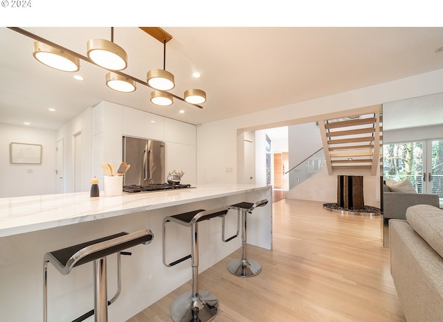 kitchen with light stone countertops, high quality fridge, white cabinets, light hardwood / wood-style floors, and a breakfast bar area