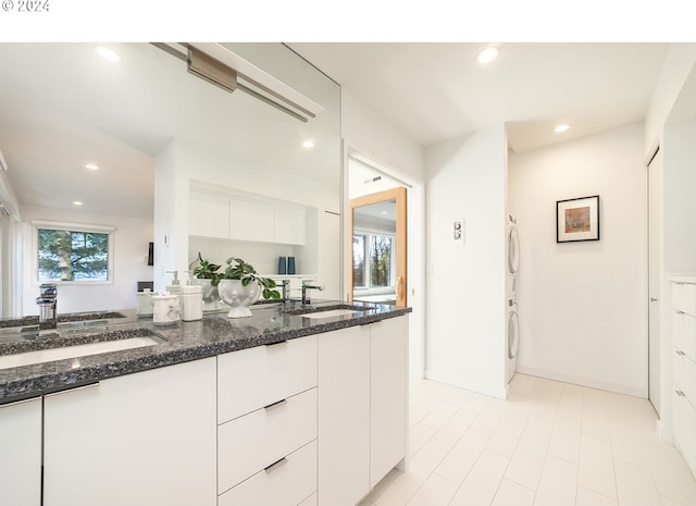 kitchen featuring stacked washer and dryer, white cabinetry, dark stone countertops, and sink