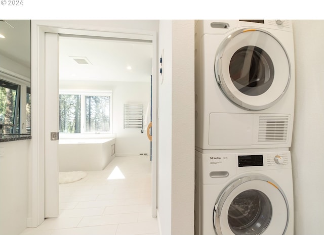 clothes washing area with a wealth of natural light, light tile patterned flooring, and stacked washer and clothes dryer