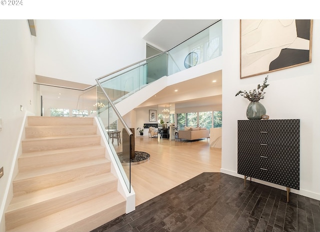 stairway featuring a notable chandelier, wood-type flooring, and a towering ceiling