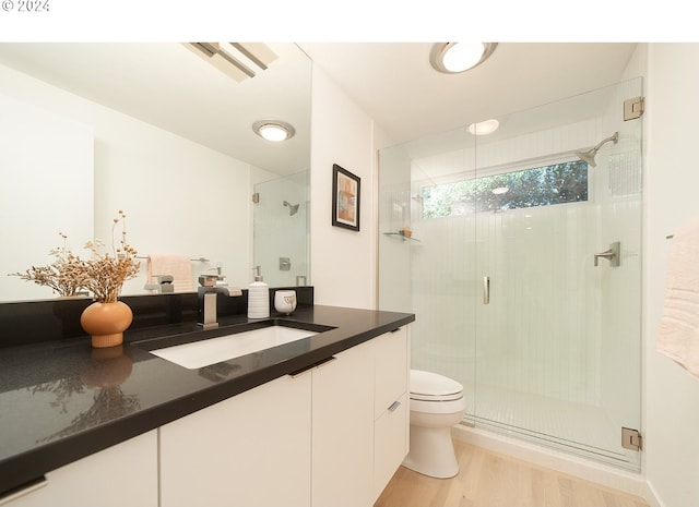 bathroom featuring vanity, wood-type flooring, a shower with shower door, and toilet