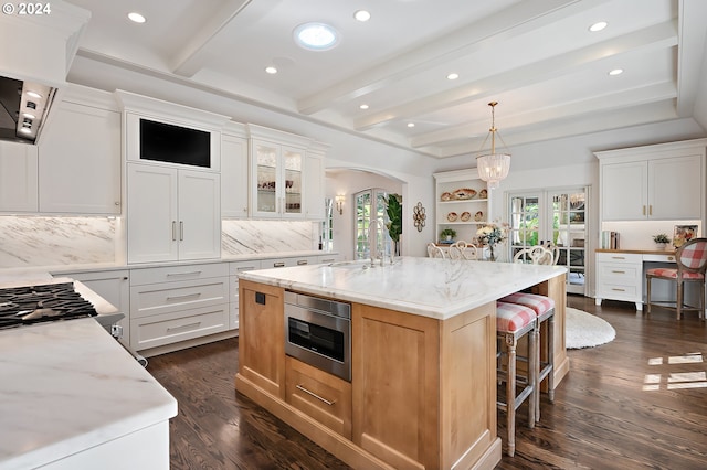 kitchen featuring stainless steel microwave, a center island with sink, beam ceiling, tasteful backsplash, and white cabinets