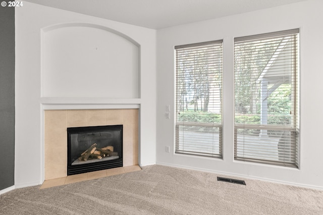 unfurnished living room featuring a tile fireplace and light colored carpet